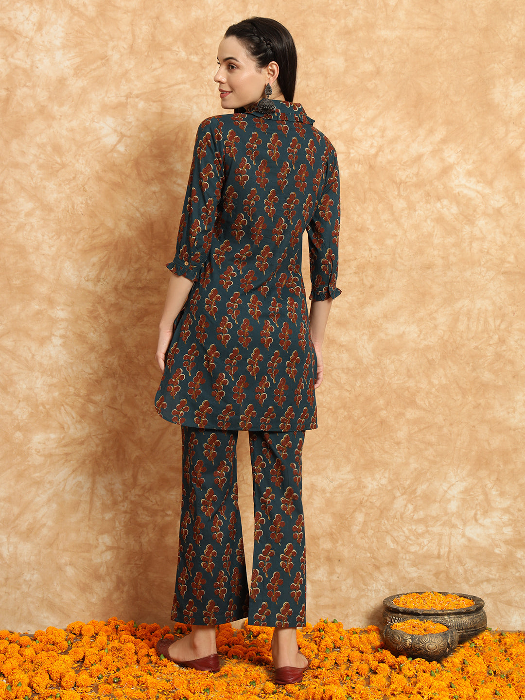 Woman in teal floral maternity kurta set with pants, standing on marigold flowers