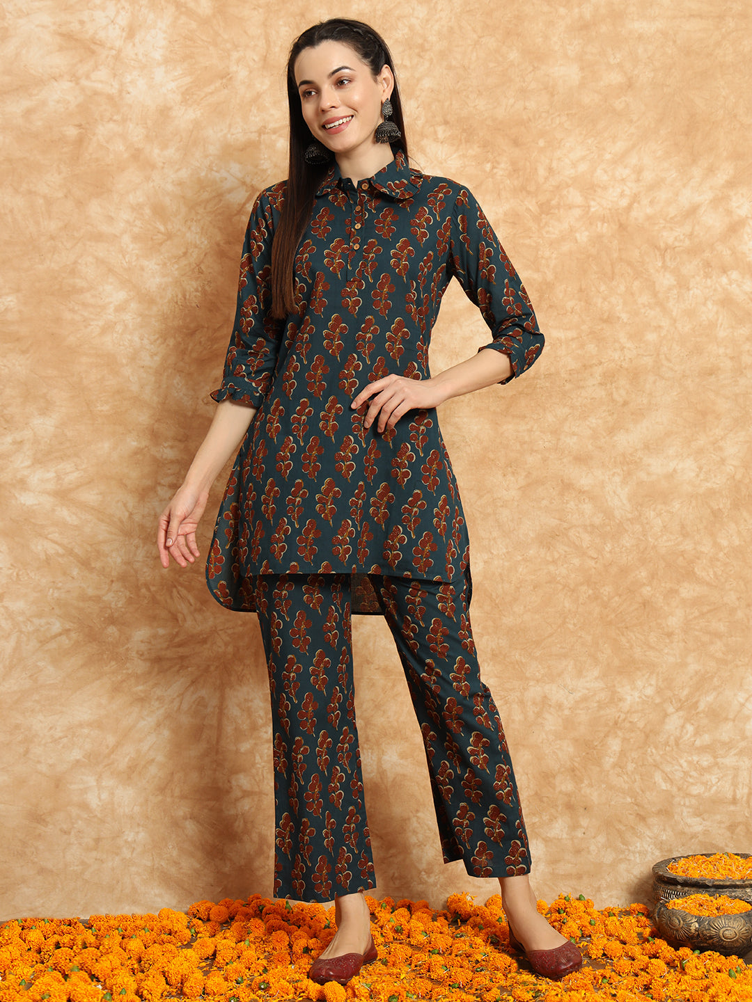 Woman wearing teal floral maternity kurta set with three-quarter sleeves, standing on marigold flowers