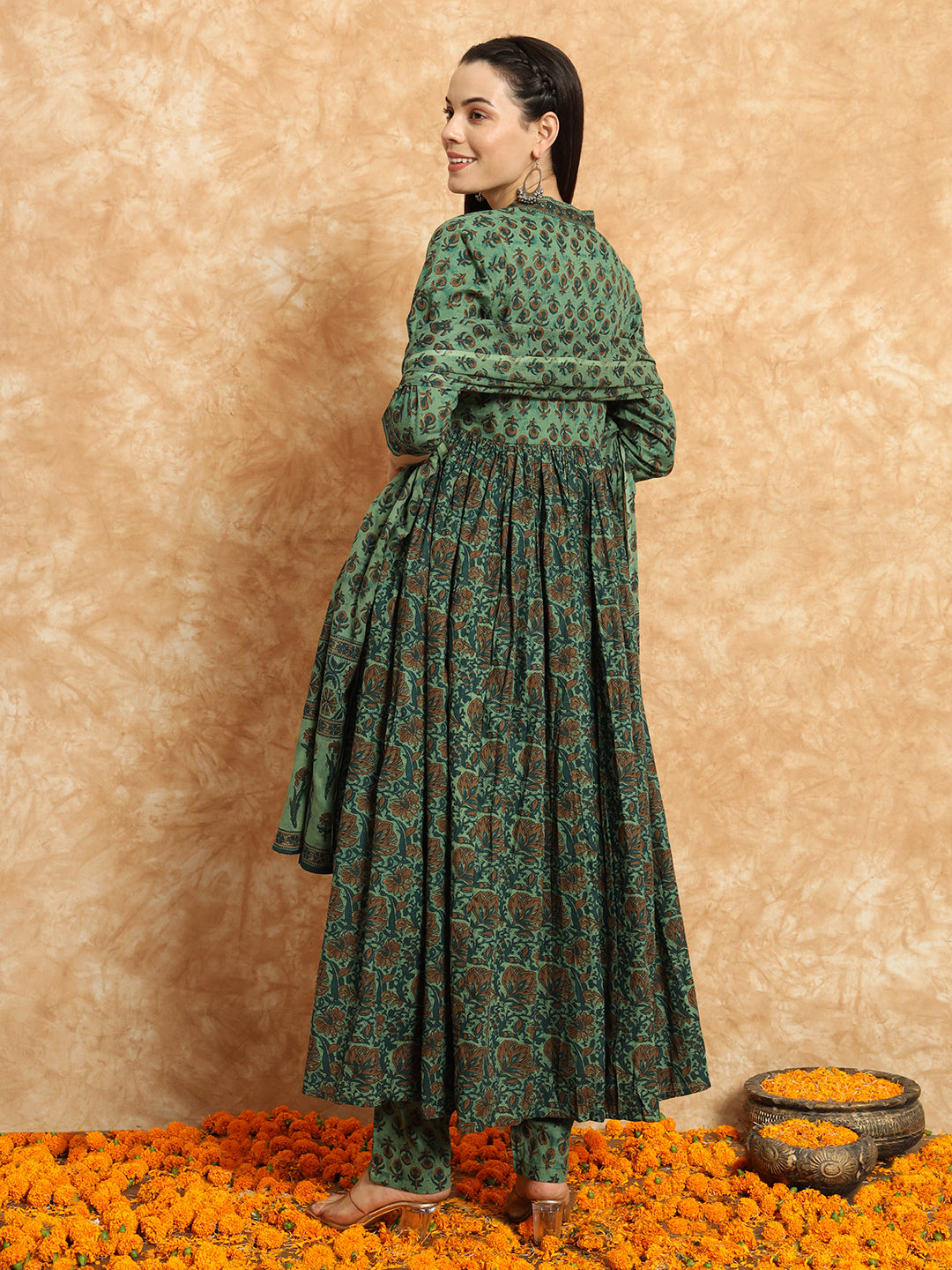 Woman in green floral maternity dress with long sleeves, standing on marigold flowers.