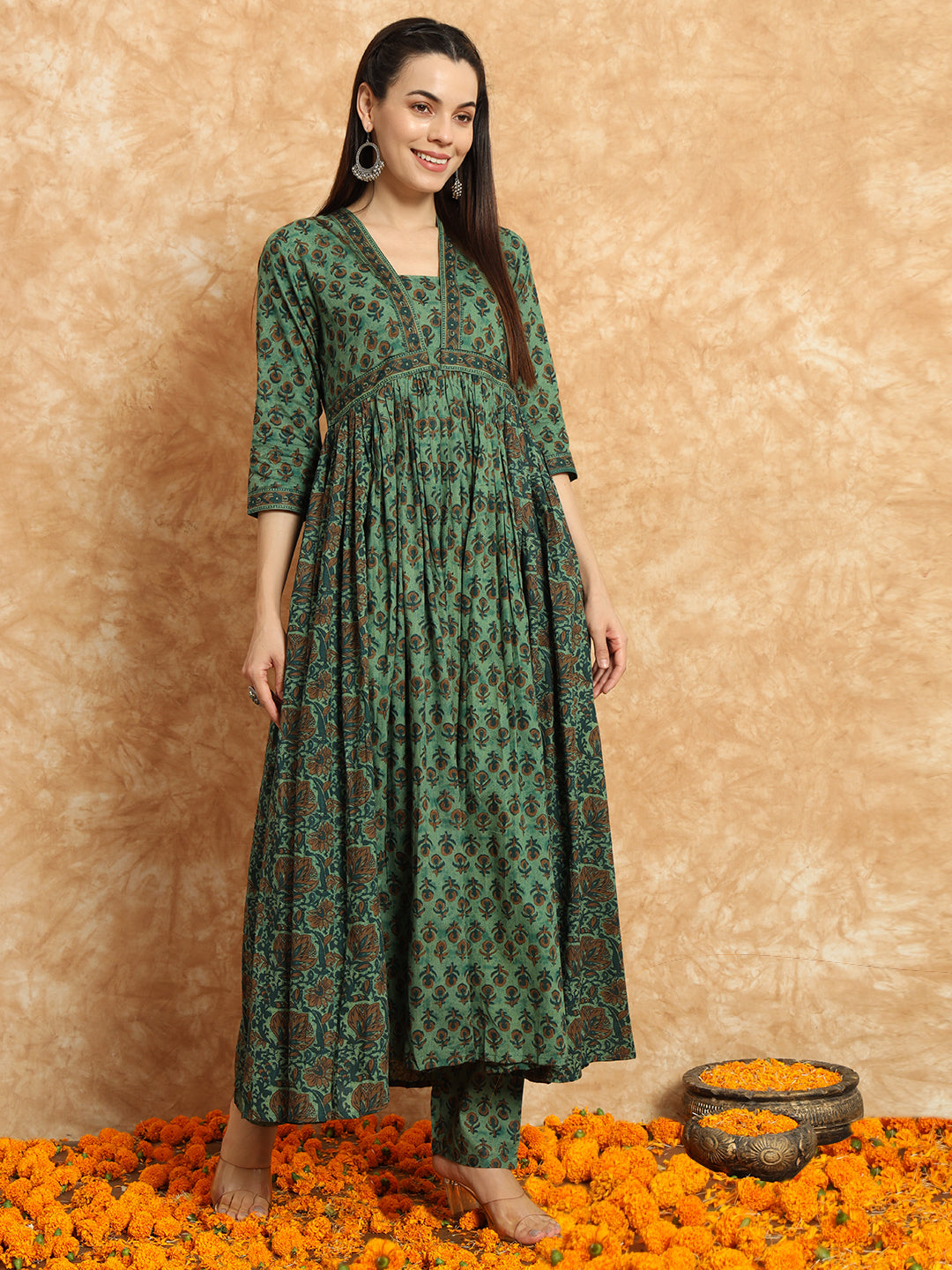 Woman wearing a green floral printed maternity kurta set, standing on marigold flowers.
