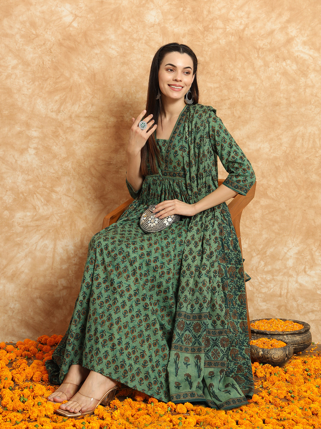 Woman in a green printed maternity maxi dress with dupatta, sitting on chair among marigold flowers