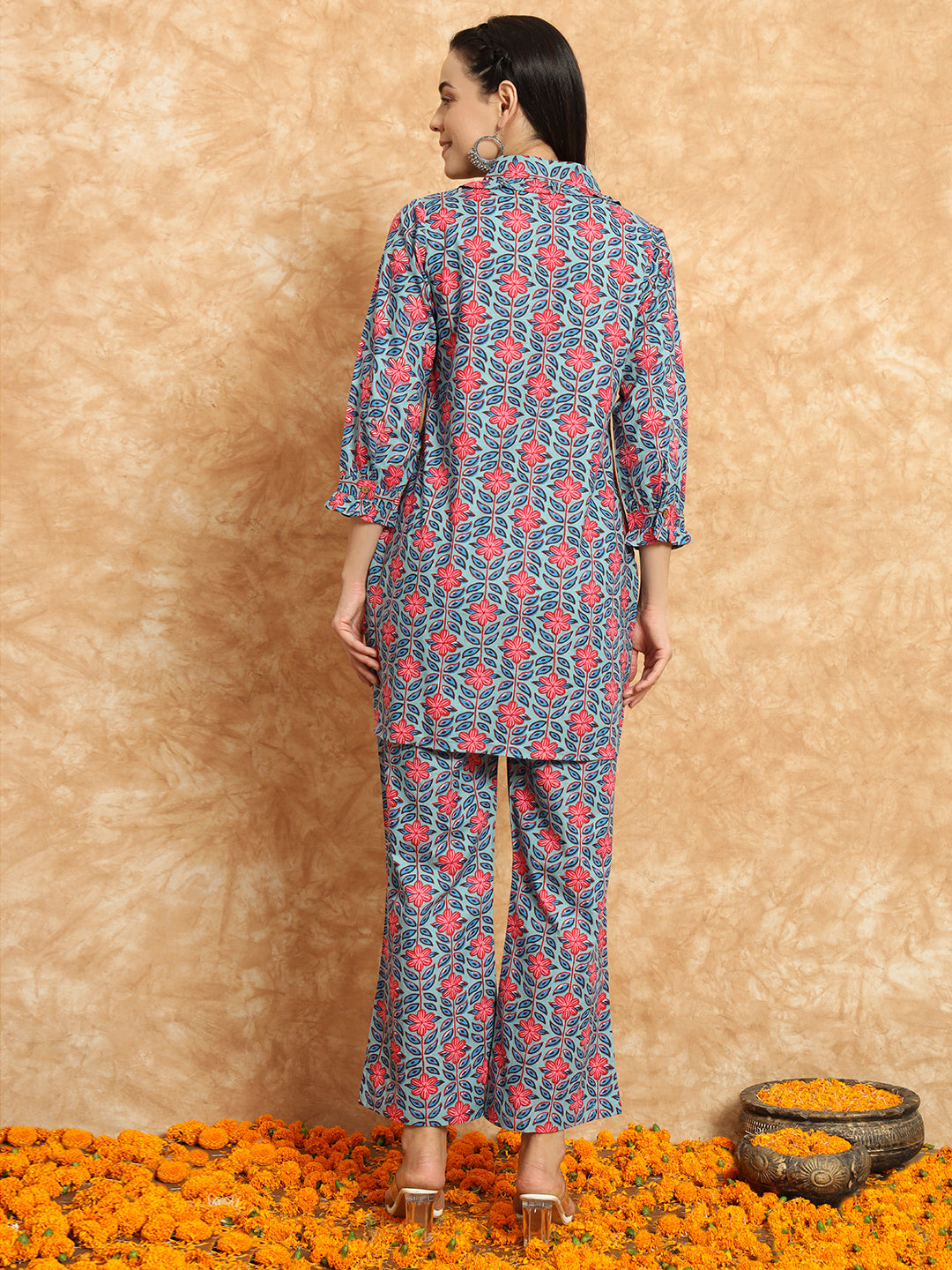 Woman in floral printed maternity kurta and pants set standing on marigold flowers indoors