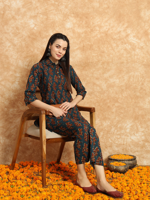 Woman in a dark floral print kurta set seated on a wooden chair amid marigold flowers