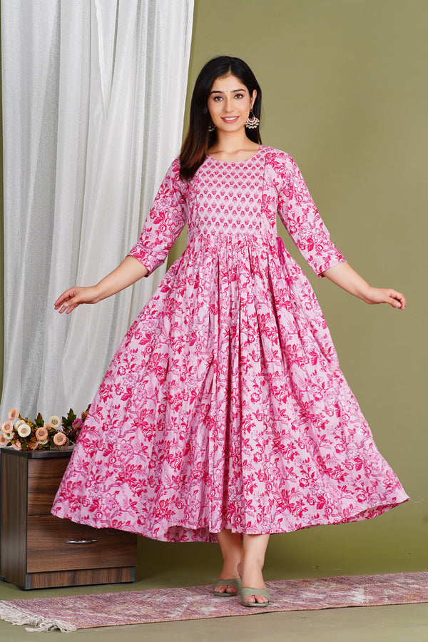 Woman wearing pink floral maternity maxi dress with three-quarter sleeves, standing indoors.