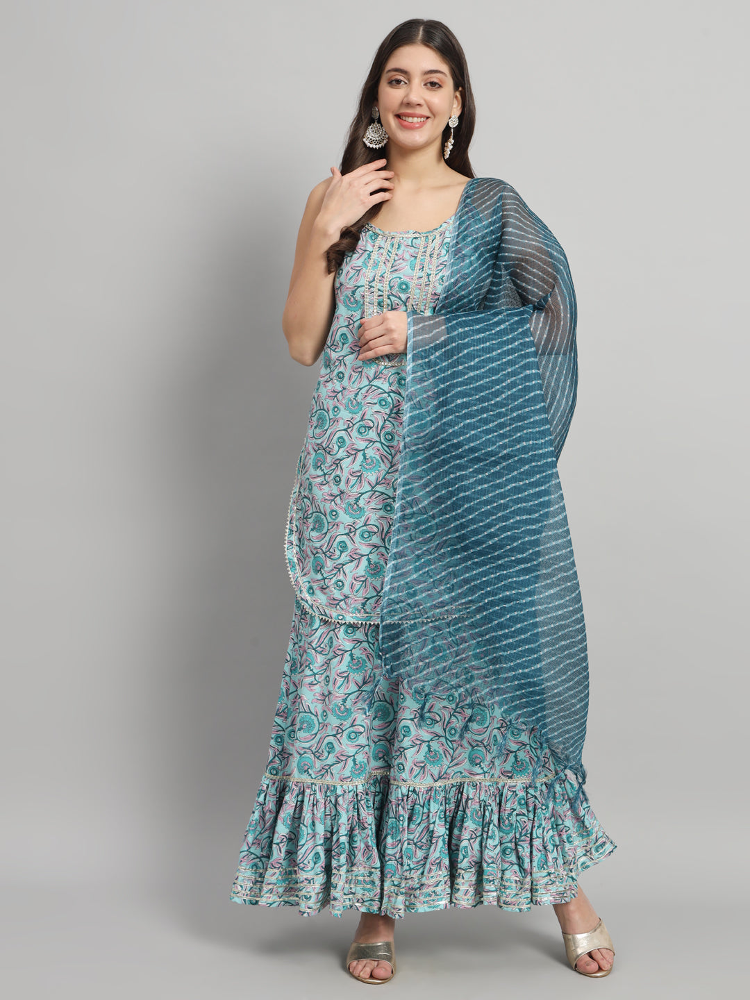 Woman in a blue floral maternity dress with dupatta, smiling and posing against a grey background