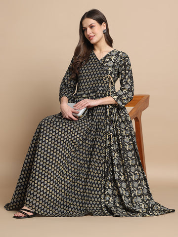 Woman in a black printed maternity dress with floral patterns, sitting cross-legged, holding a clutch.