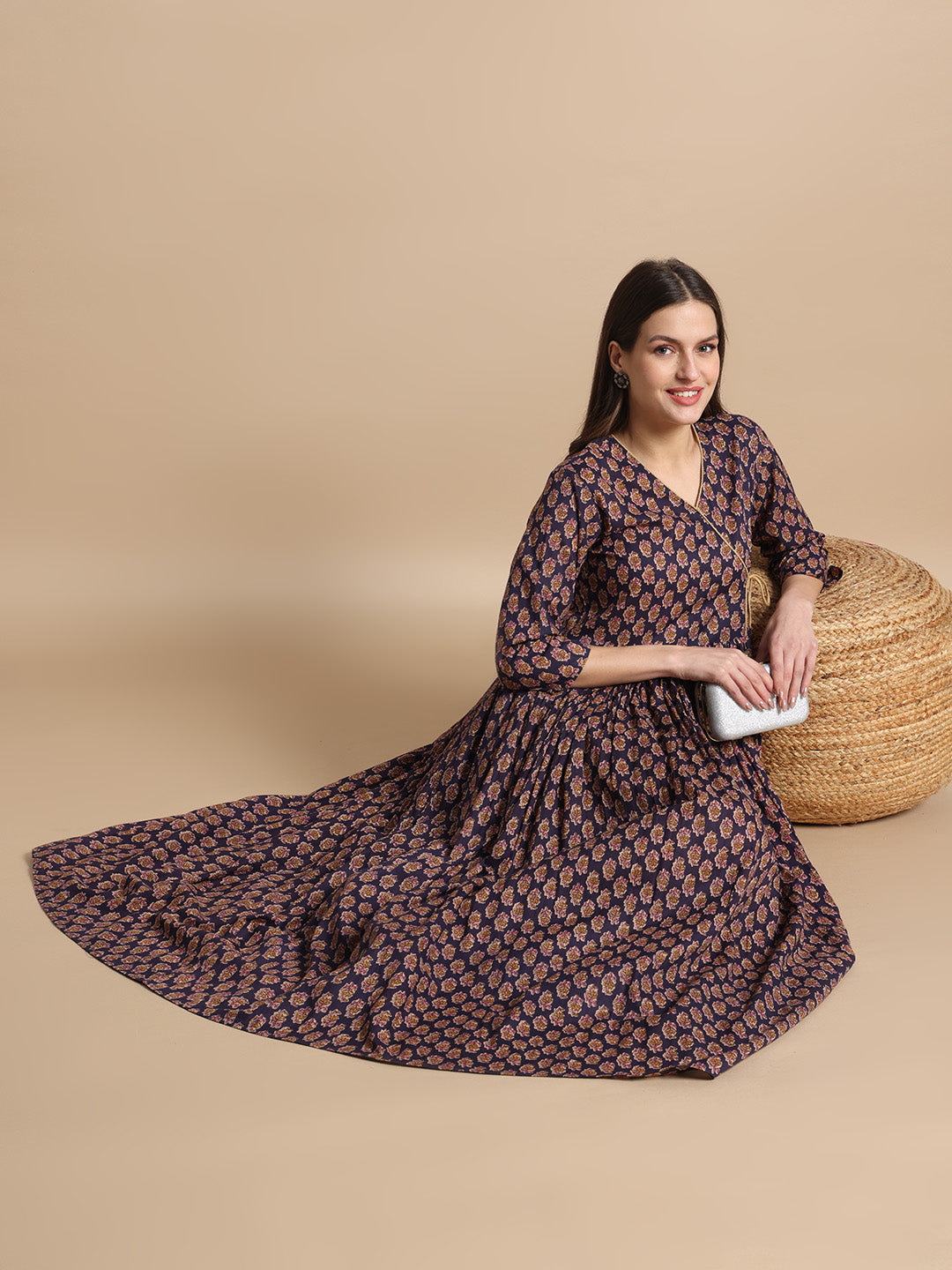 Woman in a long floral maternity dress with three-quarter sleeves, seated on beige background