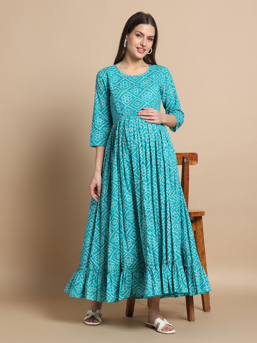 Smiling woman in teal printed maternity maxi dress with three-quarter sleeves, standing indoors