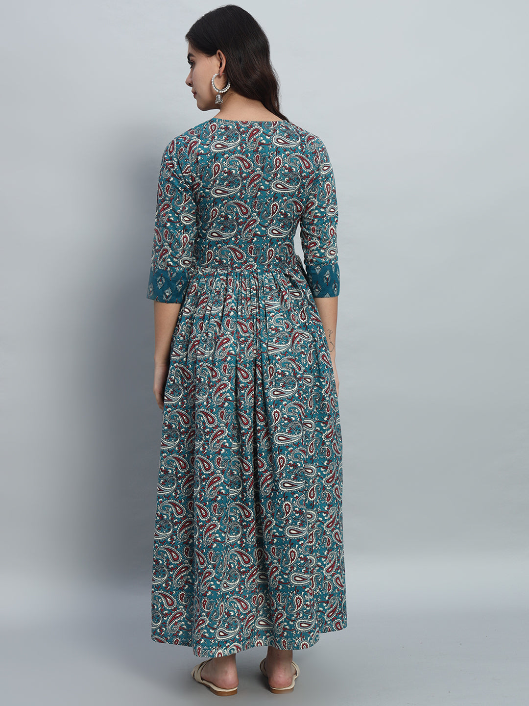 Woman wearing a teal paisley print maternity dress with three-quarter sleeves, back view
