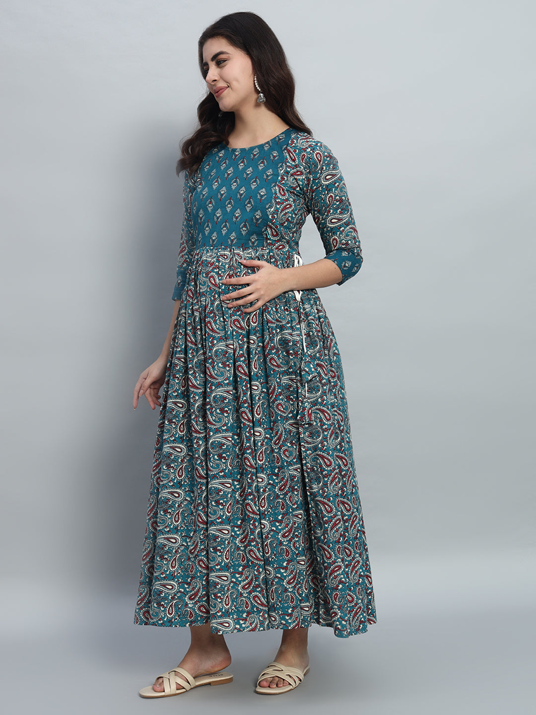 Pregnant woman wearing teal printed maternity dress with three-quarter sleeves, standing sideways.