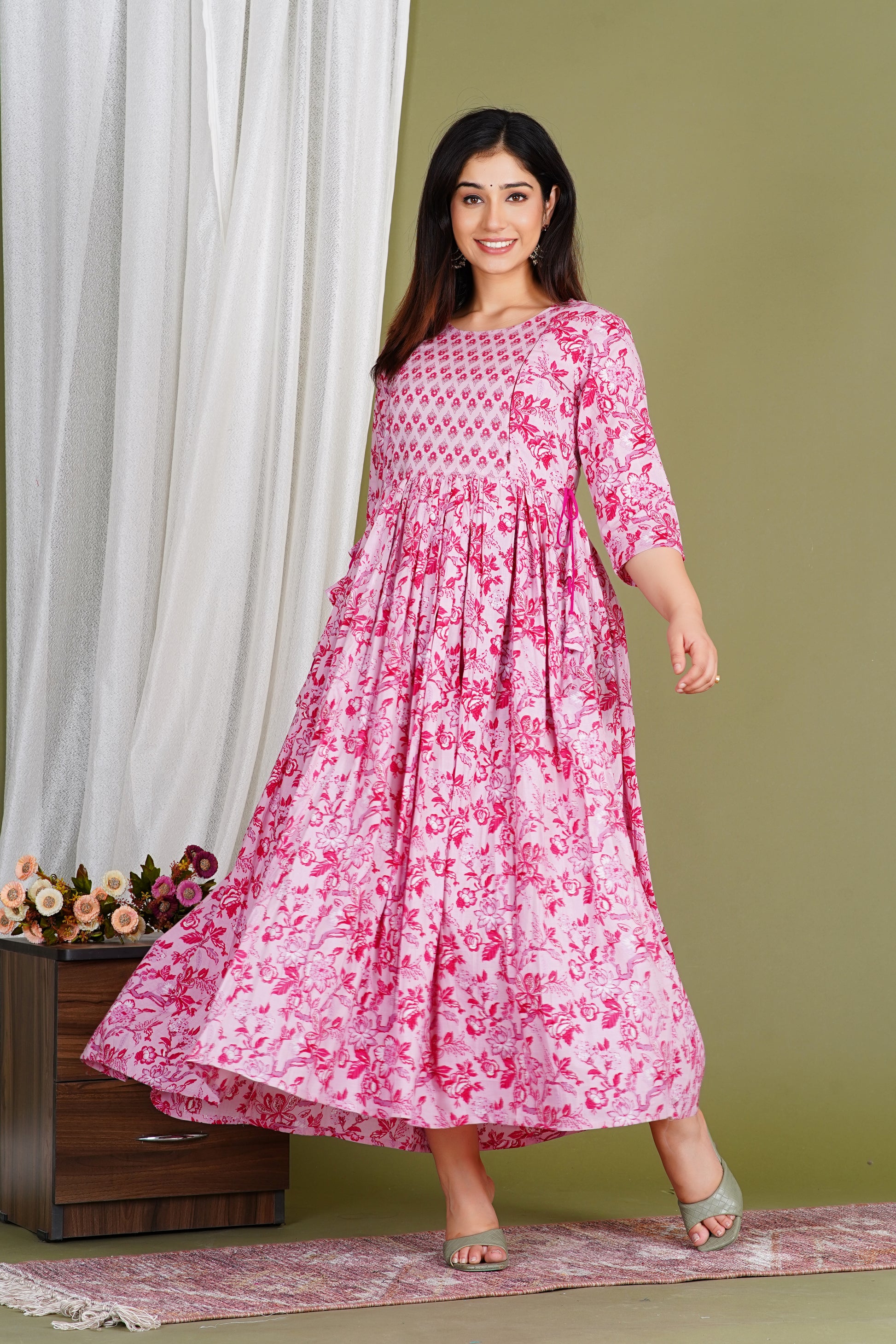 Woman wearing a pink floral maternity dress with three-quarter sleeves, standing indoors