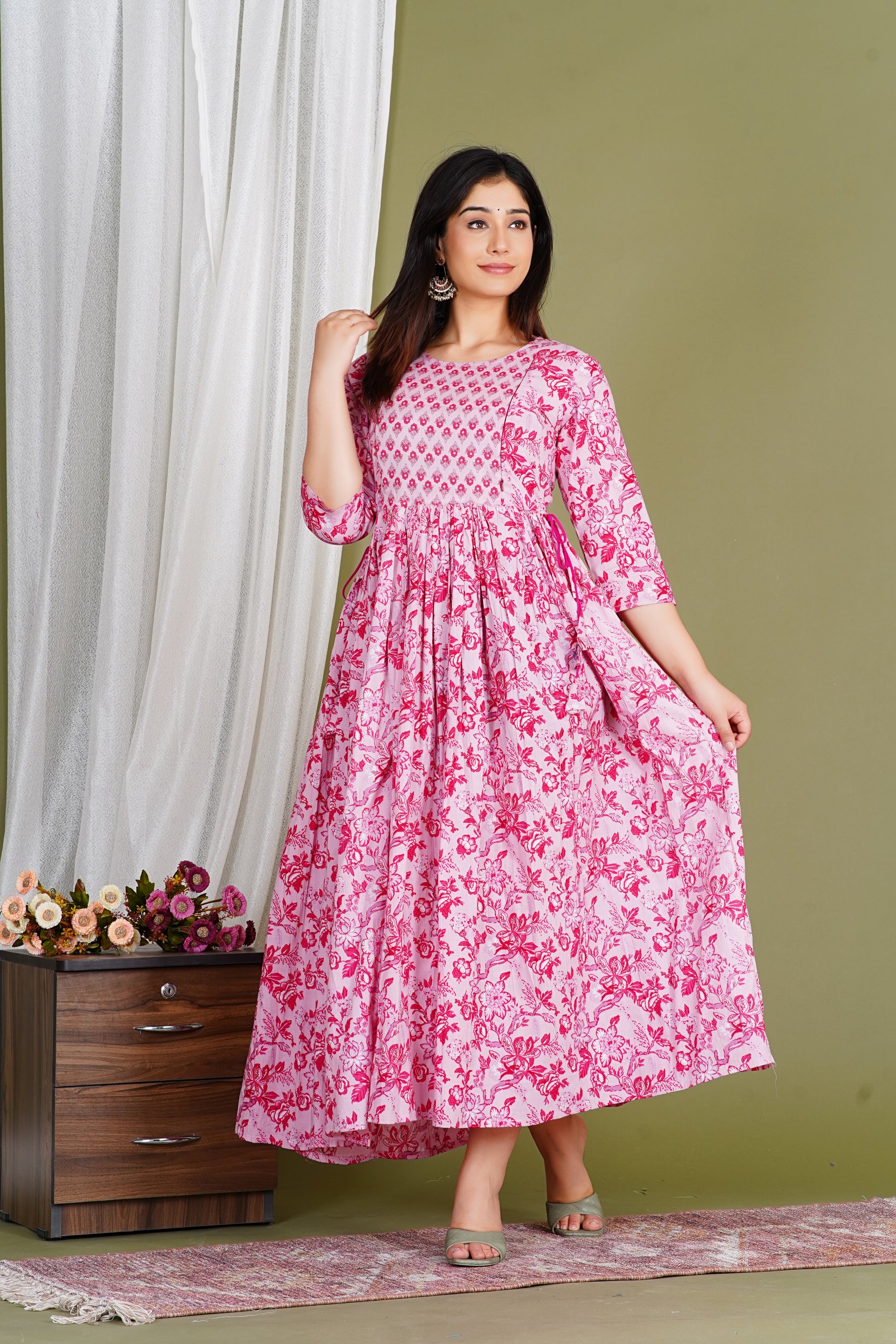 Woman in pink floral maternity dress with three-quarter sleeves, posing indoors