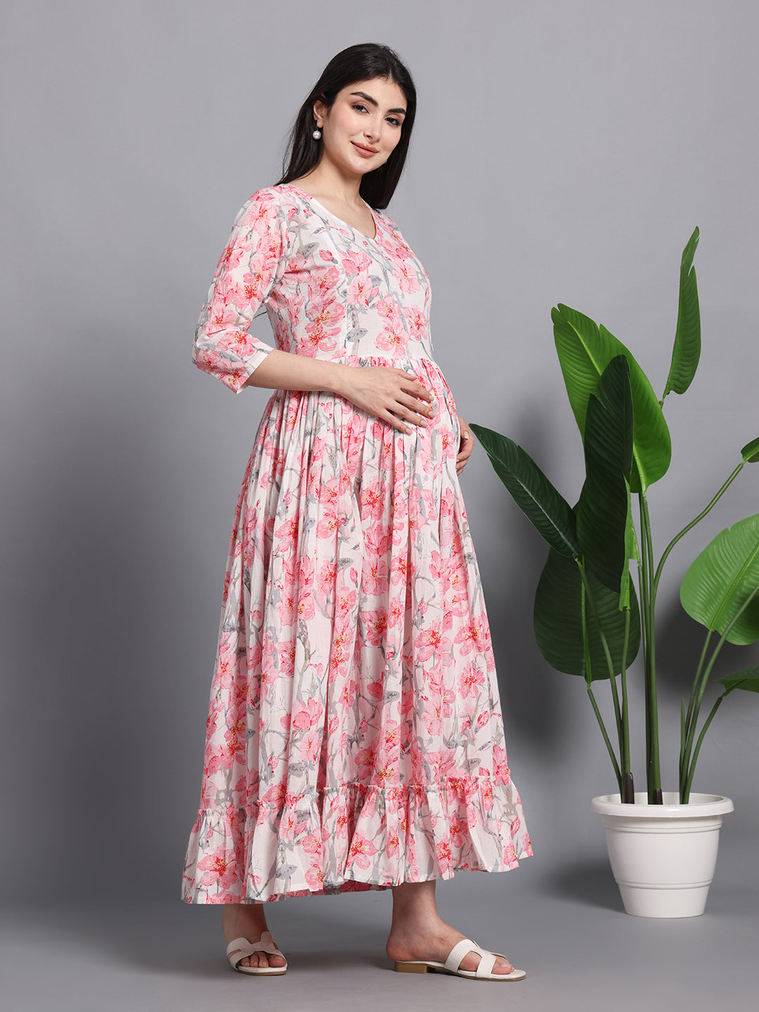 Pregnant woman in pink floral maternity maxi dress posing indoors by a potted plant