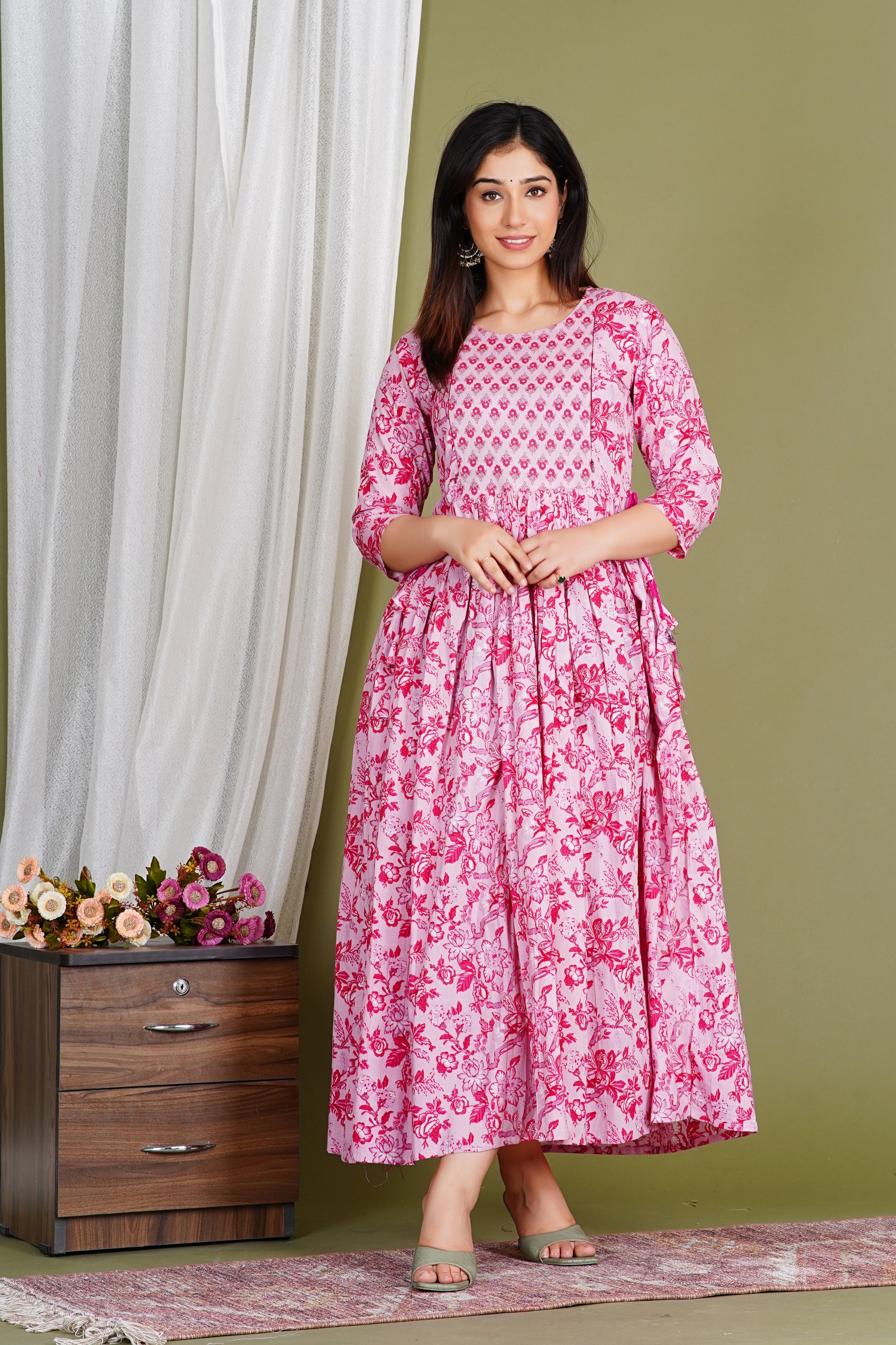 Woman wearing pink floral maternity dress with three-quarter sleeves, standing indoors