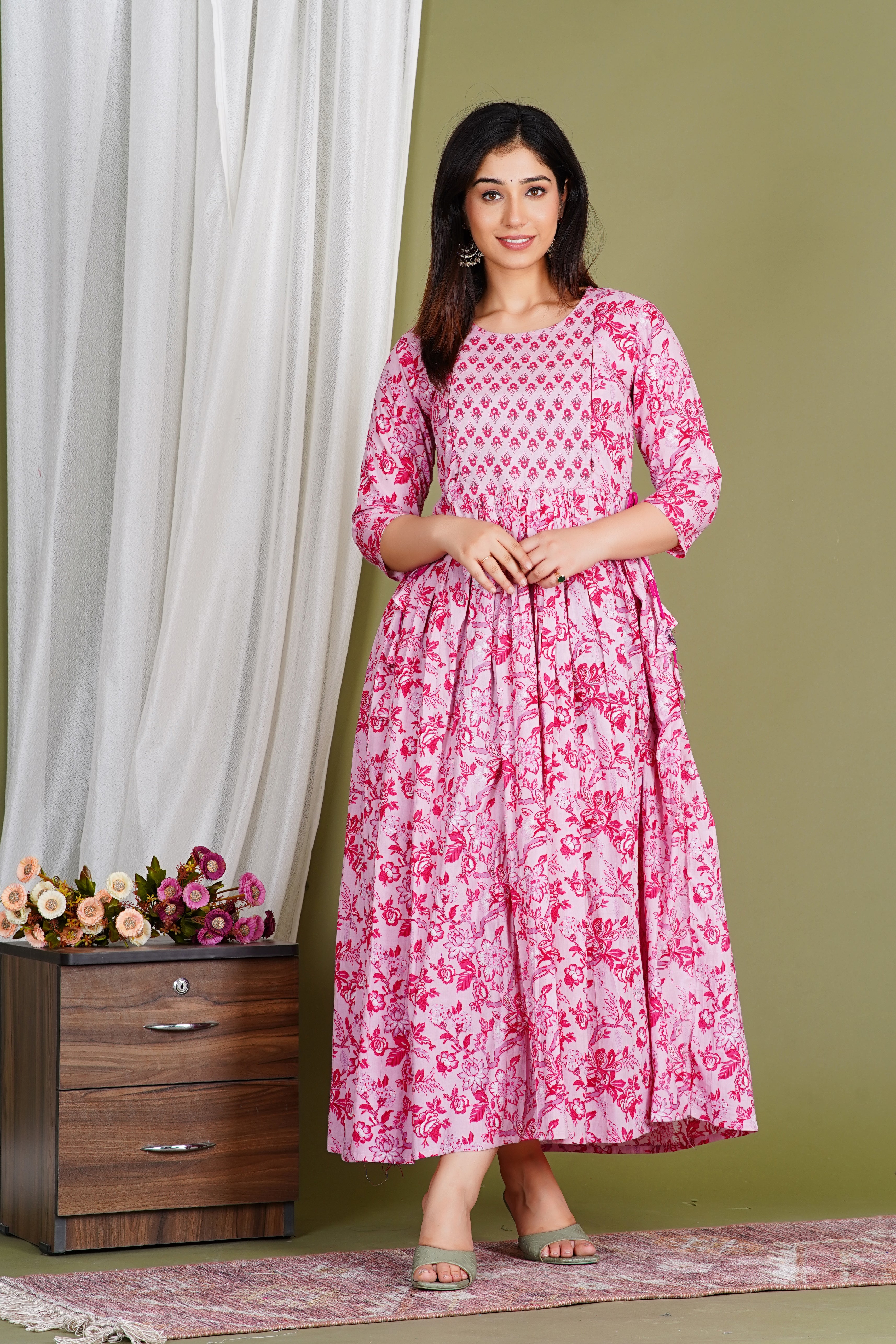 Woman wearing pink floral maternity dress with three-quarter sleeves, standing indoors