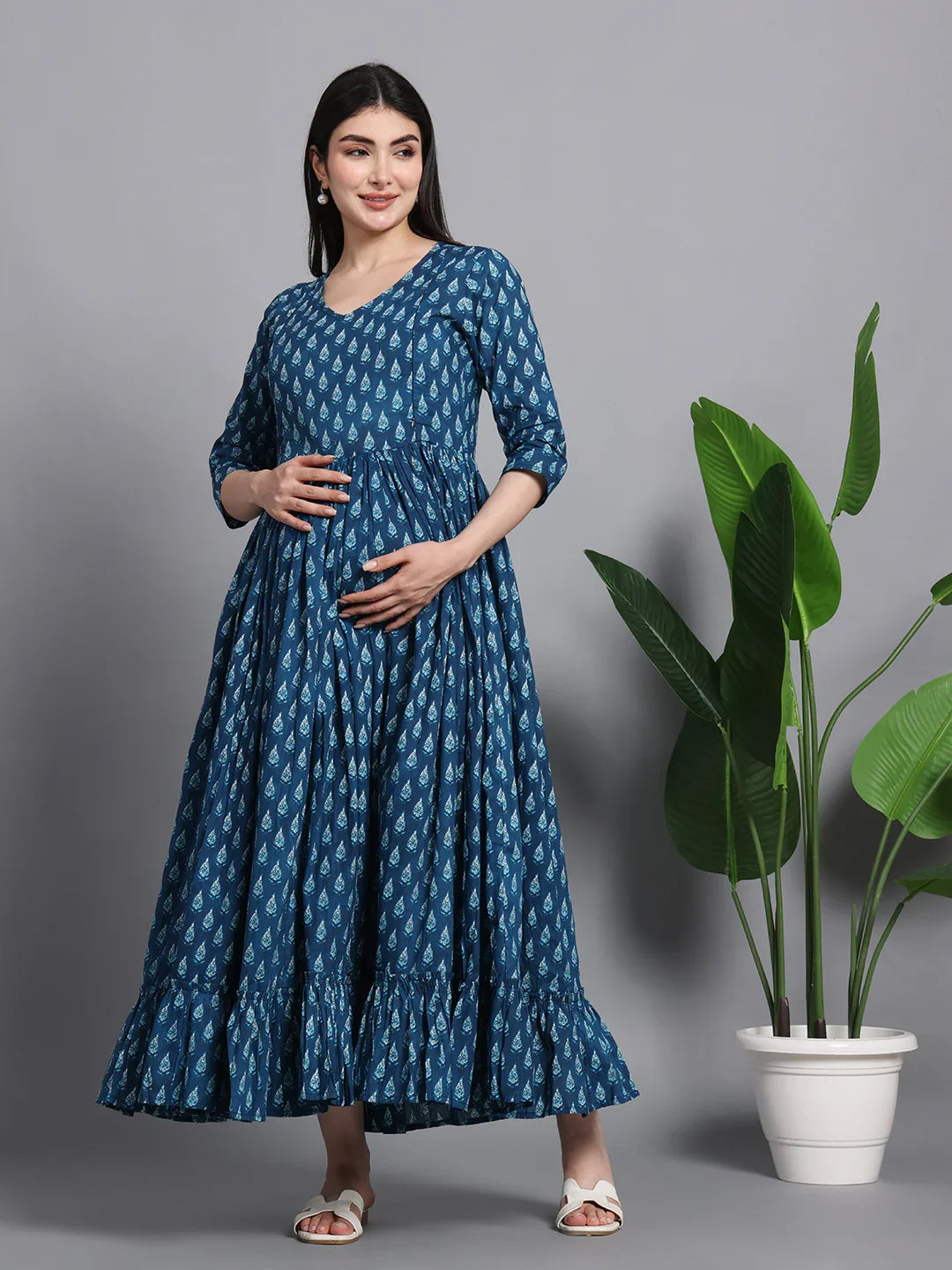 Pregnant woman in blue printed maternity dress with three-quarter sleeves standing by a potted plant