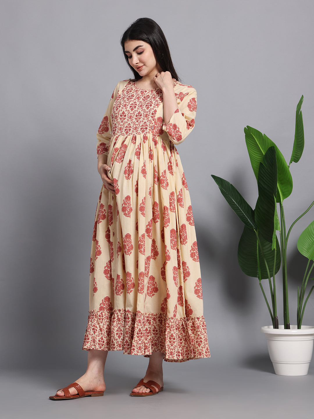 Pregnant woman wearing cream and red floral maternity dress with ruffle hem, indoor setting
