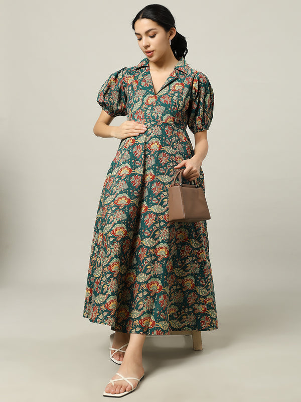 Woman wearing a green floral maternity dress with puff sleeves, holding a brown handbag