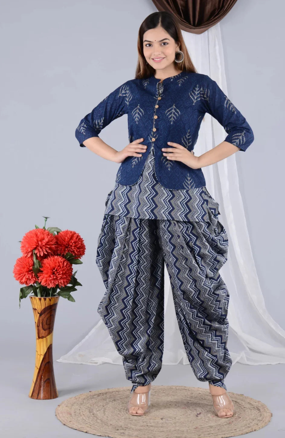 Woman wearing blue printed maternity kurta with zigzag patterned dhoti pants, standing indoors.