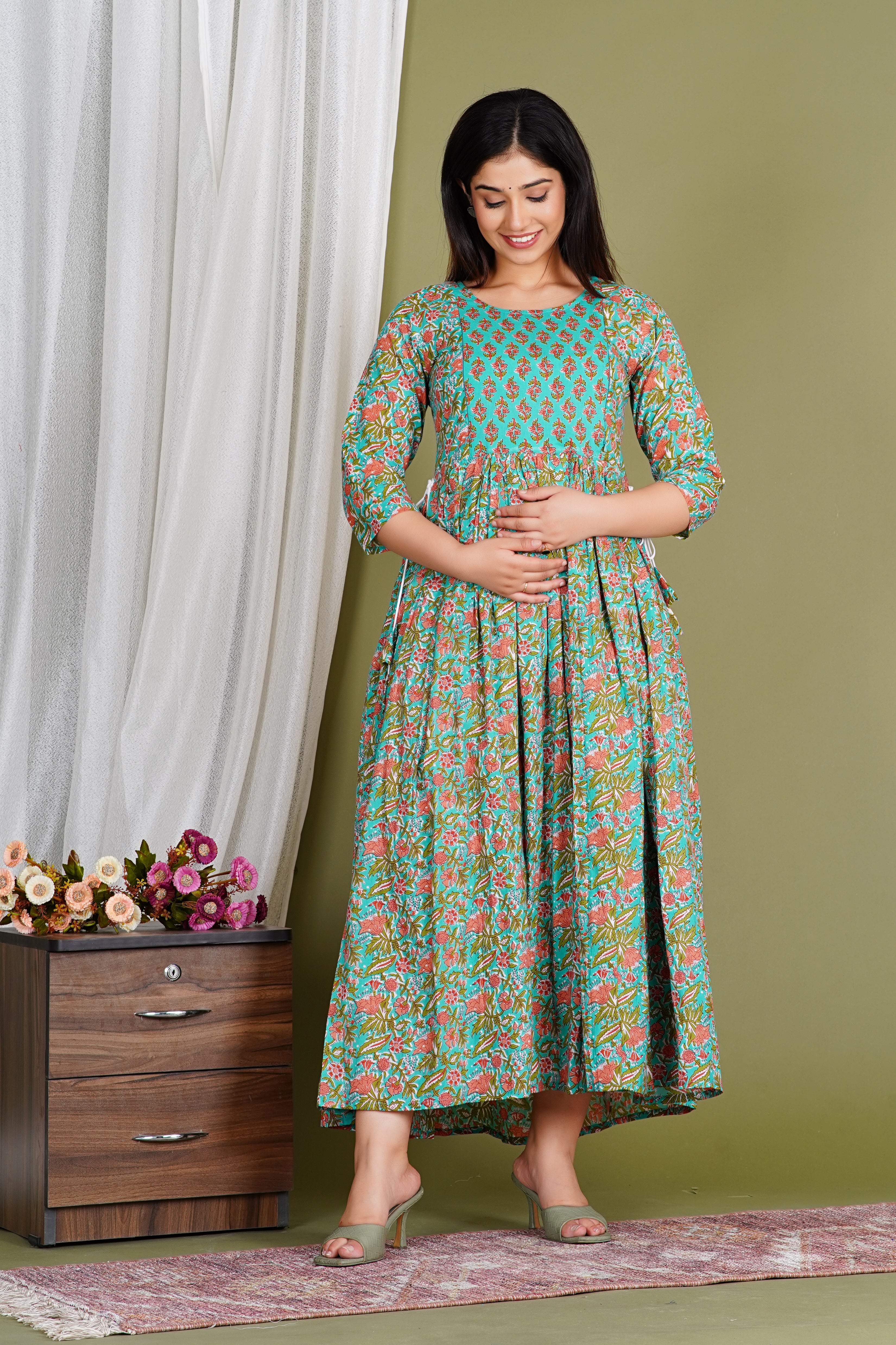 Pregnant woman in teal floral print maternity dress with three-quarter sleeves standing indoors