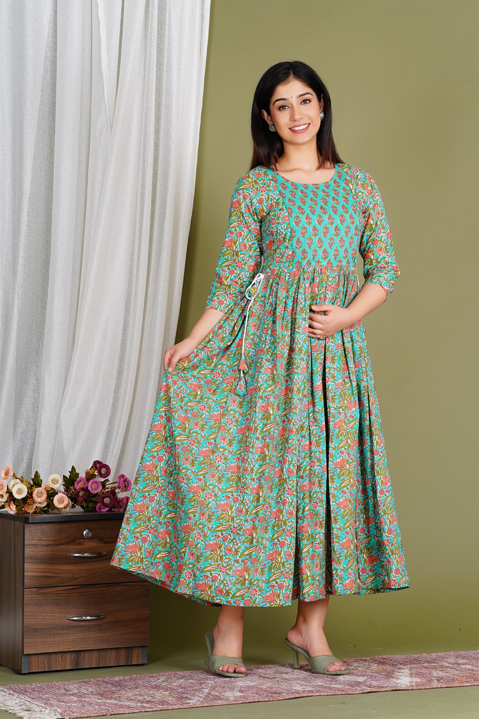Smiling woman in a teal and floral printed maternity dress with three-quarter sleeves