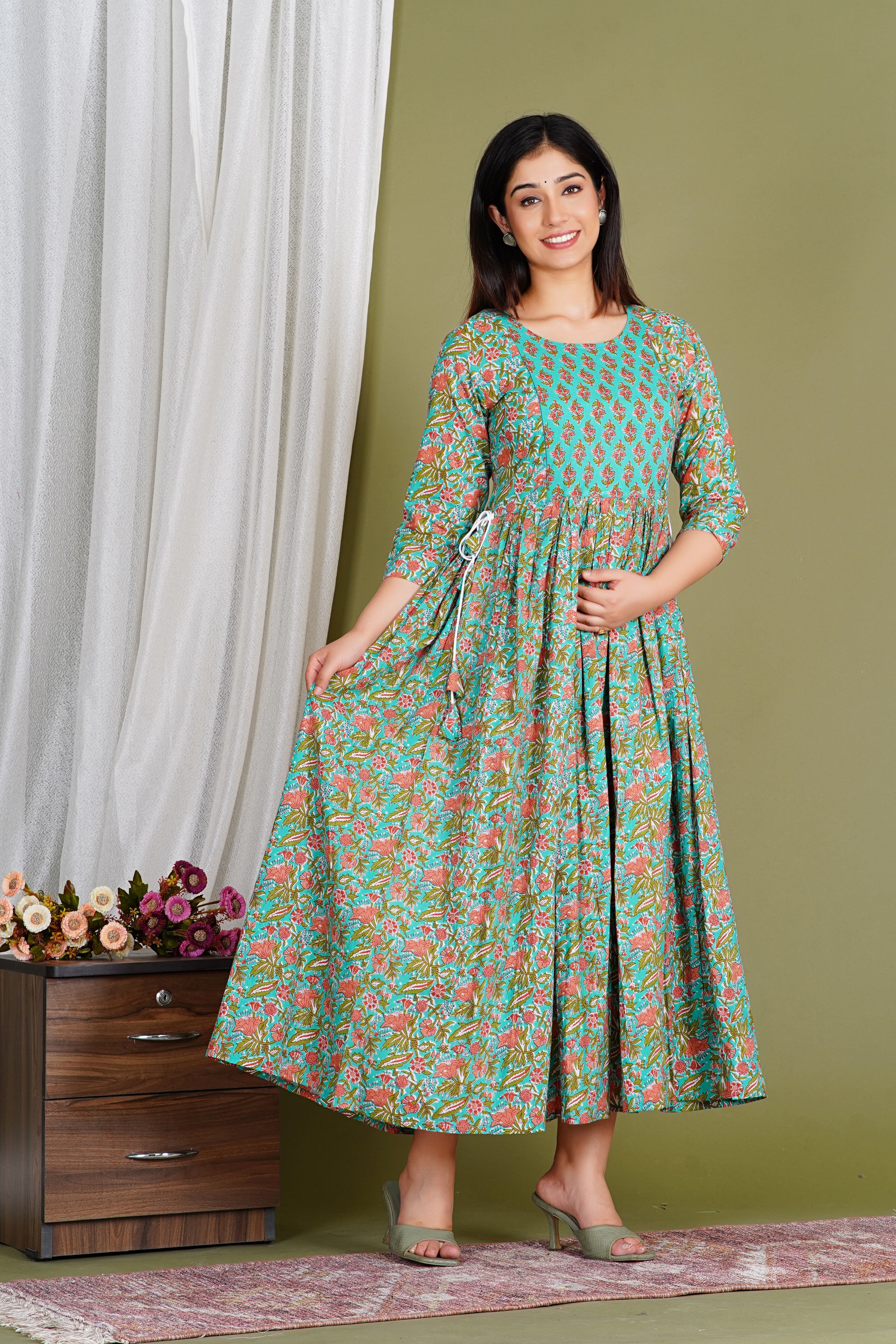 Smiling woman in a teal and floral printed maternity dress with three-quarter sleeves