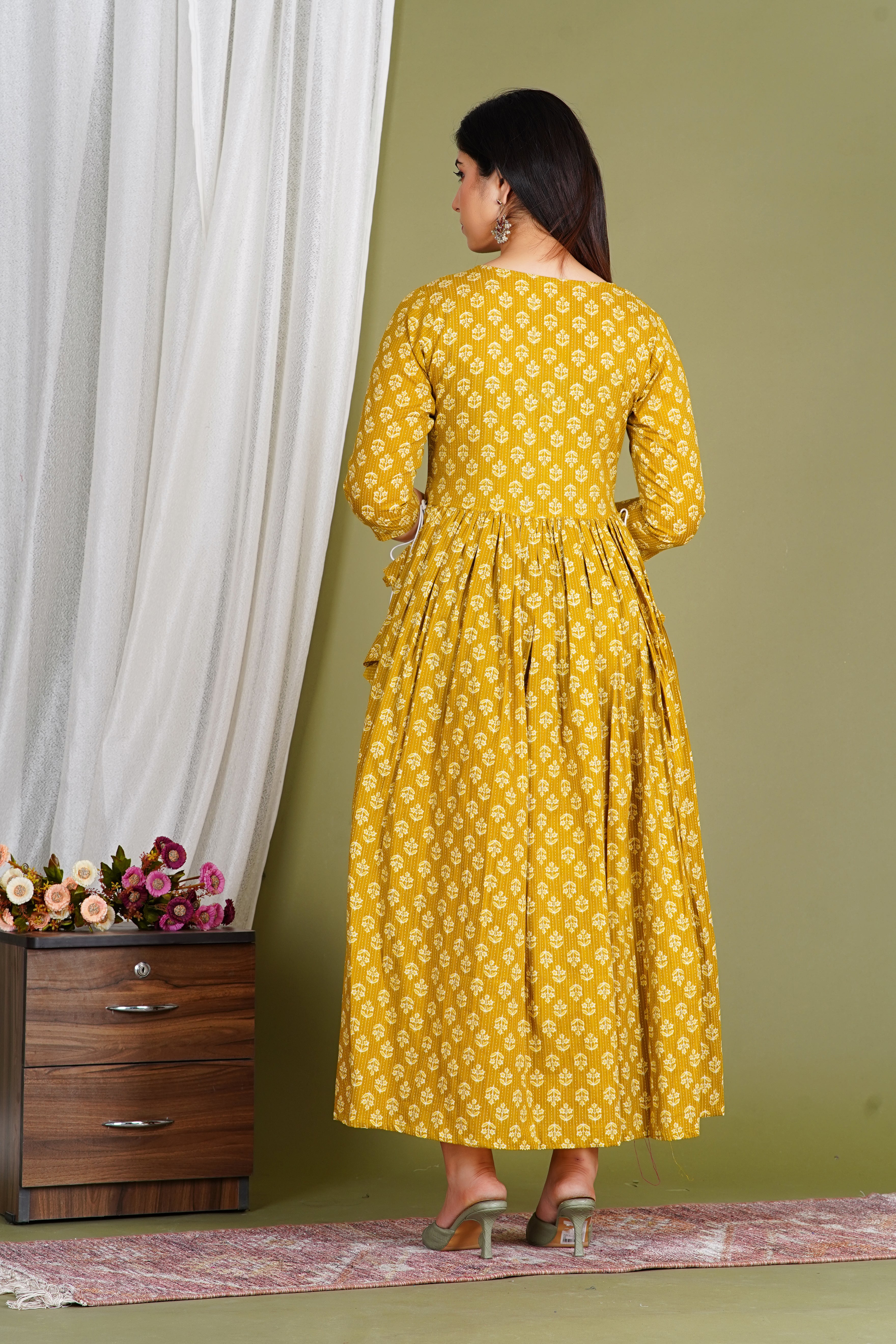 Woman in mustard yellow floral maternity maxi dress with long sleeves, standing indoors