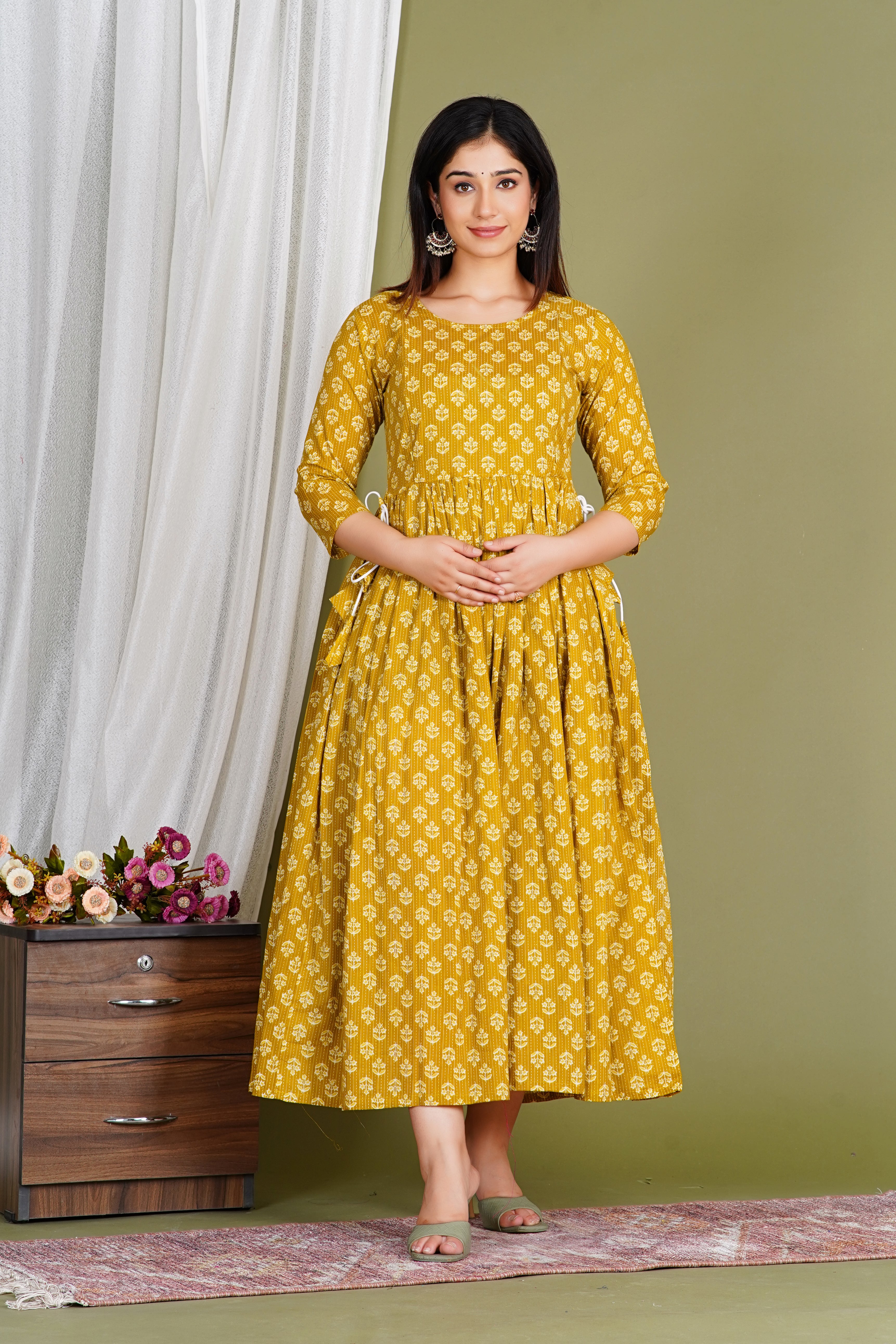 Woman in yellow printed maternity dress with three-quarter sleeves, posing indoors.